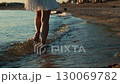 Woman walking barefoot in water on beach at sunset 130069782