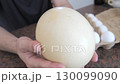 Hands holding a large ostrich egg with chicken eggs in carton nearby 130099090