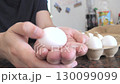 Hand Holding a White Chicken Egg Over a Kitchen Counter 130099099