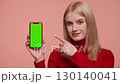 Woman pointing at smartphone with green screen isolated on pink background 130140041