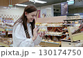 Young woman smiling while choosing fresh pastries from a supermarket shelf 130174750