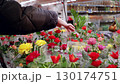 Young woman wearing a black jacket is choosing a bouquet of roses from a wide variety of colorful flowers in a supermarket 130174751