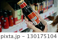 Young woman selecting a sauce bottle in a grocery store. Holding the bottle, she examines the label with focus and care 130175104
