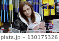 Young woman examining a stylish gray winter boot in a sporting goods store, focusing on comfort and design while selecting ideal footwear for cold weather 130175326