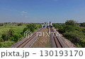 A train track surrounded by palm trees and ponds, with an overpass in the distance, on a clear day. 130193170