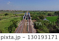 A train track surrounded by palm trees and ponds, with an overpass in the distance, on a clear day. 130193171