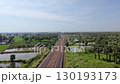 A train track surrounded by palm trees and ponds, with an overpass in the distance, on a clear day. 130193173