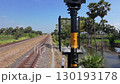 A train track surrounded by palm trees and ponds, with an overpass in the distance, on a clear day. 130193178
