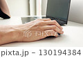 A person uses a black computer mouse while working on a laptop at a white office desk, symbolizing technology, digital work, productivity, and modern online communication 130194384