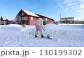 Removing snow with snow shovel held standing on snowy yard near residential building. 130199302