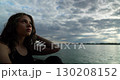 A contemplative young woman is thoughtfully sitting by the water, lost in her deep reflections 130208152