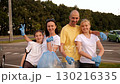 A portrait of a happy family of volunteers, wearing gloves and carrying bags of collected garbage, in a city park. They are giving a thumbs up and smiling. 130216335