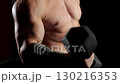 A close-up of a man in the bodybuilding pose, with his muscular arm flexing a bicep, holding black dumbbells. A professional powerlifter in action. A bodybuilder working out with black dumbbells. 130216353