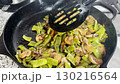 A woman stews sliced green beans and mushrooms in a cast iron skillet on the stove, preparing a healthy homemade vegetable dish with fresh ingredients 130216564