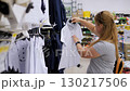 An adult mother is choosing a white school shirt for her son in a school uniform store at the mall, as they prepare for the upcoming school year. 130217506