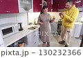 Eating orange slices with peel middle aged white couple stand in modern kitchen surrounded by appliances and bright lighting creating warm atmosphere. 130232366