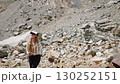 Woman hiker stops to take photo of mountain view. Blonde female in hiking outfit with cap, long hair photographs mountain landscape on phone. Outdoor adventure in rocky terrain. Slow motion. 130252151