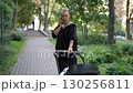 A Young Woman Happily Enjoying a Leisurely Walk with a Stroller in the Park on a Beautiful Day 130256811