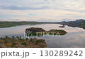 Tranquil lake with cloud reflections and rocky islands against green hills 130289242