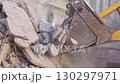 Excavator bucket lifts concrete rubble onto growing heap 130297971