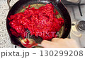 A woman is sauteing grated carrots and beets in a cast iron pan on the stove, preparing a traditional borscht base with fresh vegetables for cooking 130299208