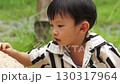 A Thai boy in black stripe shirt is having fun playing with sand alone with his hands. 130317964