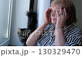 Senior woman rubbing her eyes while sitting near a window. Highlights exhaustion, aging, and the need for rest. 130329470