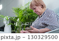 Senior woman with glasses browsing her phone while taking notes. Highlights learning, self-education, and staying informed. 130329500