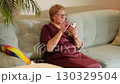 Elderly woman sitting on a couch looking at her smartphone. Highlights the growing use of technology among seniors for news and social media. 130329504