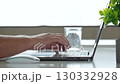 Office worker sits at work desk, typing on laptop keyboard, with glass of water and small plant nearby. Person demonstrating productivity and focus in modern workspace. Close up unrecognizable person 130332928