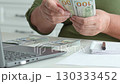 Professional accountant meticulously counting us dollar banknotes. Writing financial details on notepad with laptop and smartphone nearby. Capturing focused financial analysis and management workflow 130333452