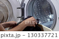 female hand loading black laundry into the drum of a home washing machine. woman with basket doing laundry 130337721