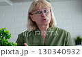 Video call with students or relatives. Online learning. Old people freelancing. Elderly woman with glasses and green shirt is speaking explaining or teaching something, looking directly at the camera 130340932