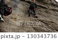 Two climbers scaling vertical rock wall with ropes and harnesses on challenging outdoor cliff face against bright sky 130343736