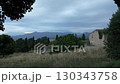 Stone farmhouse with ivy-covered walls in rural meadow under cloudy evening sky with mountain range in the distance 130343758