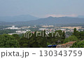 Panoramic view of Girona cityscape with lush trees in foreground and layered Pyrenees mountain range in soft blue haze under clear summer sky 130343759