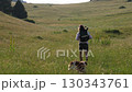 Adult man hiking with loyal dog through green summer meadow under bright daylight 130343761