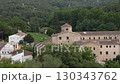 Historic stone monastery complex with tiled roofs surrounded by lush green forest and village houses in scenic countryside landscape 130343762