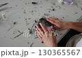 Female hands arranging lavender stems on white table, creating bouquet with scattered flowers and herbs, emphasizing lavender crafting as calming and artistic activity. Hands tying lavender bouquet 130365567