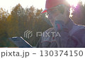 Builder is arguing with customer, solving problems. Construction engineer wearing orange safety helmet and glasses is making phone call while reading a document on a clipboard. 130374150