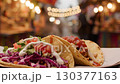 Mouthwatering street tacos are displayed with vibrant toppings and sauces in an outdoor market. The atmosphere is lively with lights and people enjoying the evening 130377163
