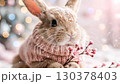 Adorable bunny wearing a pink knitted sweater holds a small flower branch. Soft, light colors create a cheerful atmosphere perfect for winter celebrations 130378403