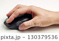 A person hand holds a black computer mouse on a white desk near a laptop, symbolising technology, navigation, internet use, office work, and digital productivity 130379536