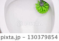 Close up of a person cleaning a toilet bowl with a green brush, scrubbing to remove dirt and stains, maintaining bathroom hygiene, sanitation, and household cleanliness 130379854