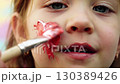 Young boy playfully smears red paint on his face in a close up shot	 130389426