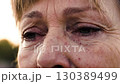 Close up of a mature woman's face with wrinkles opening and closing her eyes	 130389499