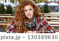 Young woman with curly hair poses casually in an outdoor setting during autumn fashion event 130389630