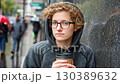 Young adult with curly hair and glasses holding a coffee cup in urban setting during rainy day 130389632