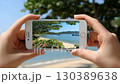 Capturing a serene beach view with hands holding a smartphone during a sunny day in a coastal paradise 130389638