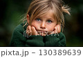 Child with thoughtful expression resting chin on hands in a natural setting during late afternoon light 130389639